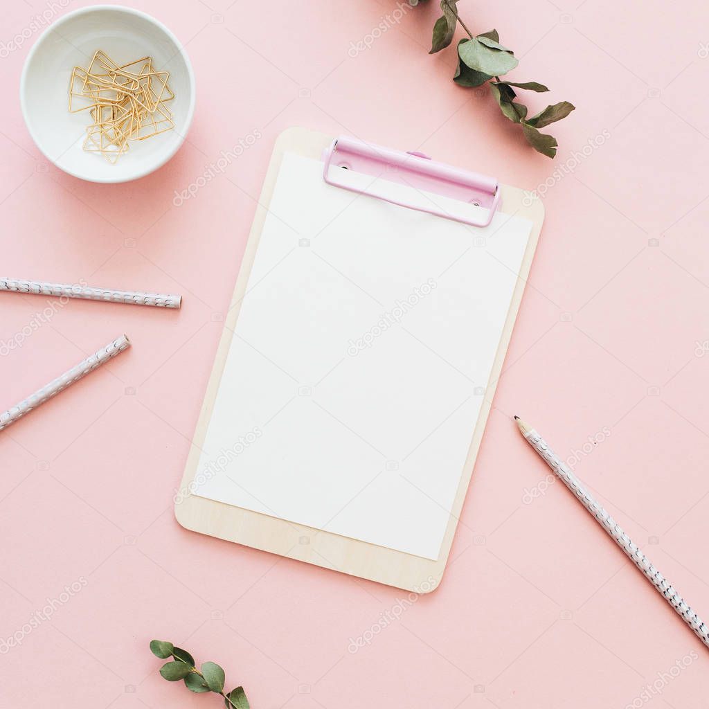 Flat lay office workspace with blank clipboard, eucalyptus branches on pink background. Top view minimal mock up template concept.