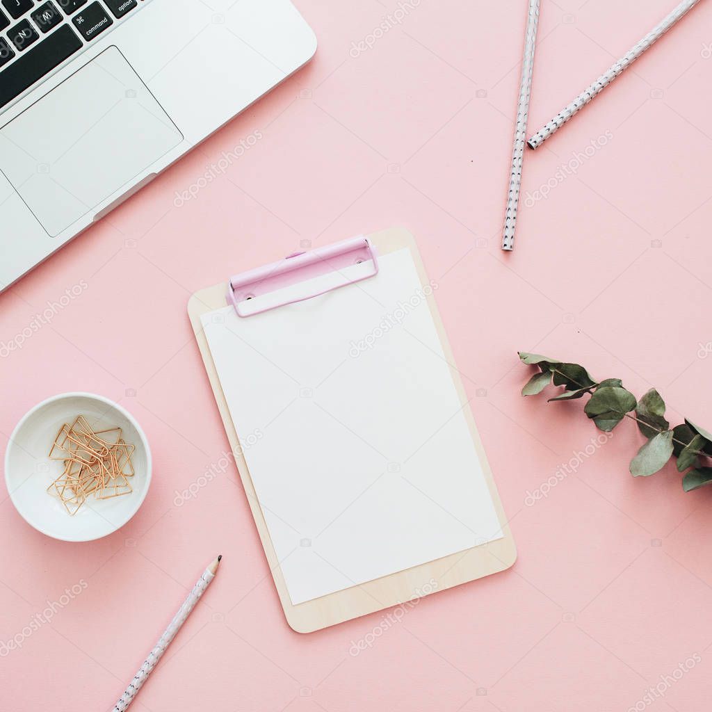 Flat lay office workspace with blank laptop, clipboard, eucalyptus branches on pink background. Top view minimal mock up template concept.