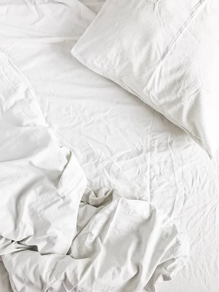 Flat lay of white bed with pillows, blanket and sheet. Top view minimal linen concept.