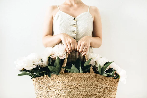 Genç hasır çanta beyaz şakayık çiçekleri beyaz arka planda tutan kadın çok. Çiçekçiler Süsleme kavramı.
