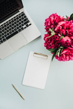 Kadın çalışma alanı laptop, pano, çiçek buketi ve aksesuarları üzerinde mavi arka plan ile. Düz yatıyordu, en iyi görünümü.
