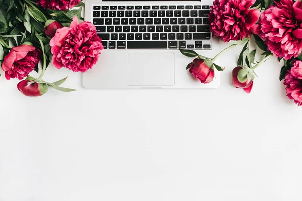 Laptop and pink peonies flowers on white background. Flat lay, top view summer background.