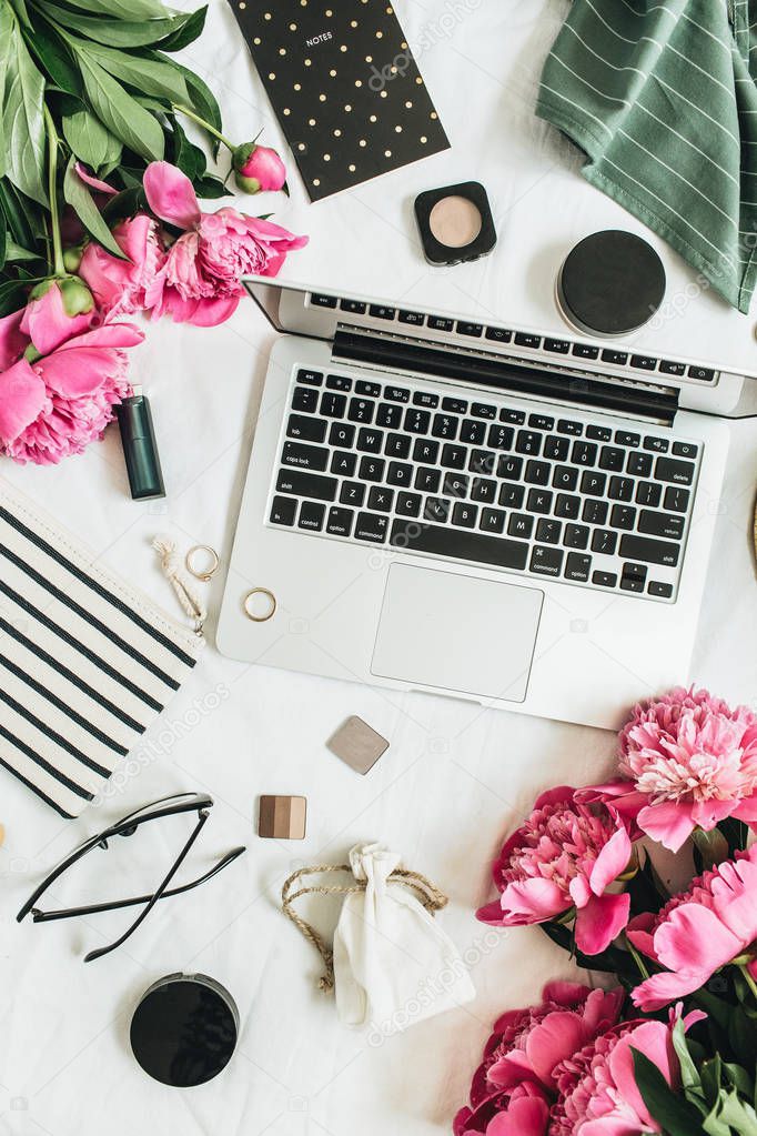 Flat lay styled fashion feminine office desk with laptop, pink peony flowers, cosmetics, accessories. Top view blog or social media background.