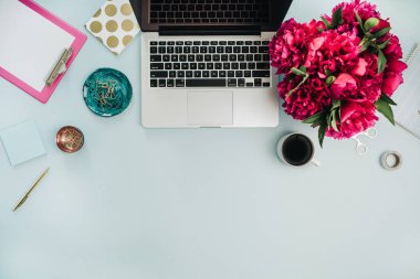 Çalışma alanı dizüstü ve pembe şakayık ile mavi arka plan üzerinde buket çiçekler. Düz yatıyordu, en iyi görünüm ev ofis masası.