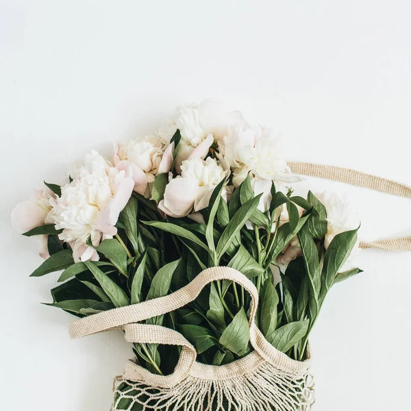 ひも付きの袋は白い背景の上に白い牡丹の花 フラット横たわっていた トップ ビュー最小限花コンセプト — ストック写真