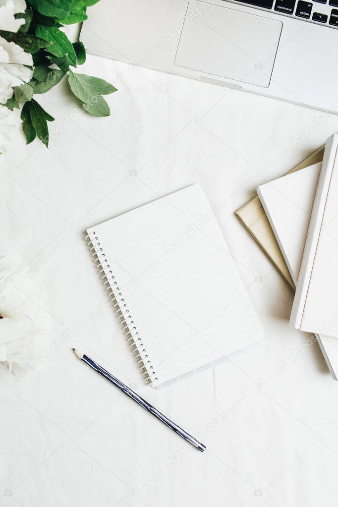 Home office workspace with laptop, notebook, white peonies flowers bouquet on white background. Flat lay, top view.