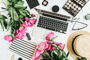 Düz yatıyordu moda kadınsı ofis büro dizüstü, pembe şakayık çiçekleri, kozmetik, aksesuarlar ile. Üstten görünüm natürmort blogger arka plan.