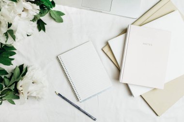 Laptop, defter, beyaz arka plan üzerinde beyaz peonies çiçekler Buket ile düz yatıyordu ev ofis masası. Üstten görünüm.