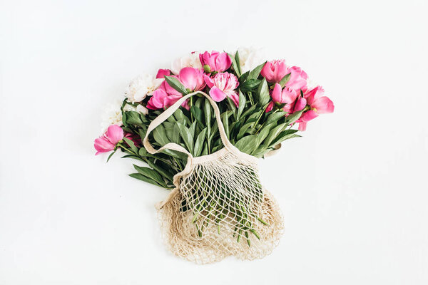 Pink and white peony flowers in string bag on white background. Flat lay, top view minimal floral concept.