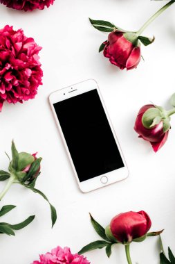 Beyaz arka plan üzerinde pembe peonies çiçeklerin çerçevesindeki akıllı telefon. Düz yatıyordu, en iyi görünümü kadar sahte.