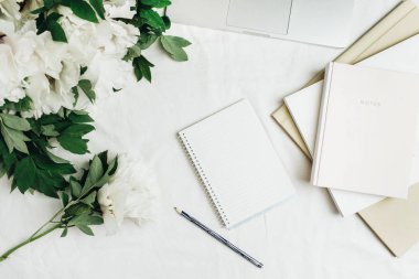 Ev ofis çalışma alanıyla laptop, defter, beyaz arka plan üzerinde beyaz peonies çiçek buketi. Düz yatıyordu, en iyi görünümü.