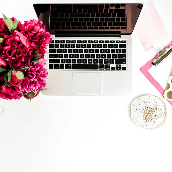 Home office desk workspace with laptop, pink peonies flowers bouquet on white background. Flat lay, top view.