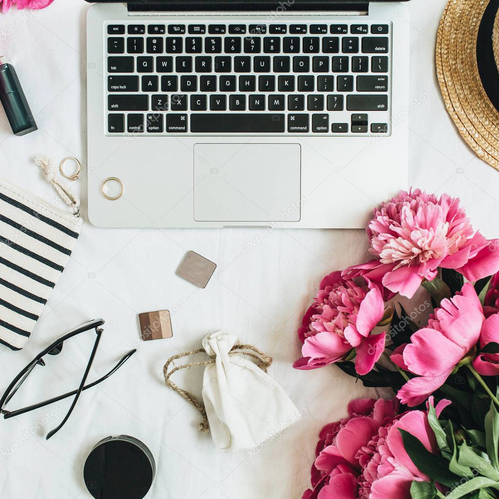 Flat lay fashion feminine office desk with laptop, pink peony flowers, cosmetics, accessories. Top view fashion or beauty blog summer floral background.