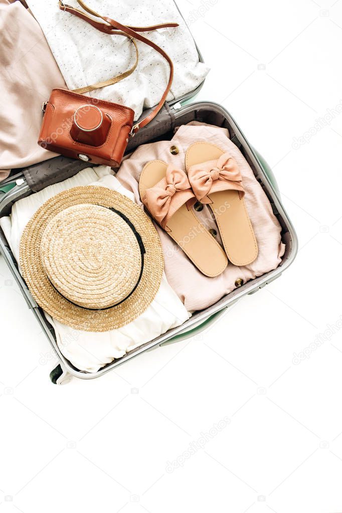 Hand luggage with feminine straw, slippers and retro camera on white background. Flat lay, top view. Summer fashion clothes and travel concept.
