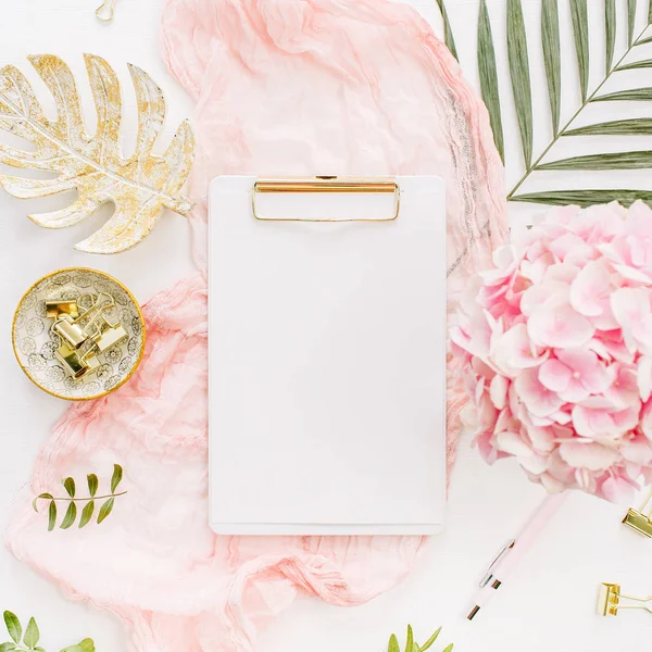 Modern ev ofis resepsiyon çalışma alanı boş kağıt Pano, pembe ortanca çiçek buketi, tropikal palmiye yaprağı, pastel battaniye, monstera yaprak plaka ve beyaz arka plan üzerinde aksesuarları ile. Düz yatıyordu, en iyi görünümü altın mockup gül.
