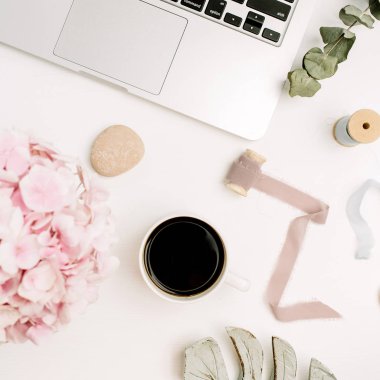 Beyaz arka plan üzerinde modern ev ofis büro. Dizüstü bilgisayar, kahve kupa, pembe ortanca çiçek buketi, okaliptüs, monstera. Düz yatıyordu, en iyi görünümü kadın blogger çalışma alanı.