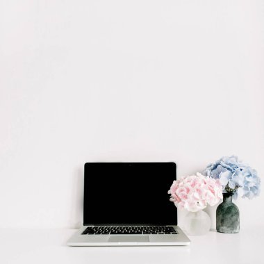 Boş ekran laptop ve pembe ve mavi ortanca çiçek buketleri beyaz arka plan üzerinde. Çok az ev ofis resepsiyon çalışma alanı.
