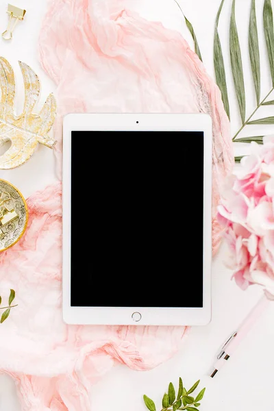 Modern ev ofis resepsiyon çalışma alanı boş ekran tablet, tropikal palmiye yaprağı, pastel battaniye, monstera yaprak plaka ve beyaz arka plan üzerinde aksesuarları ile. Düz yatıyordu, en iyi görünümü altın mockup gül.