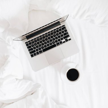 Sabah kavramı çalışma. Laptop ve kahve beyaz çarşaflar üzerinde yatakta. Düz yatıyordu, en iyi görünümü minimalist çalışma alanı arka plan.