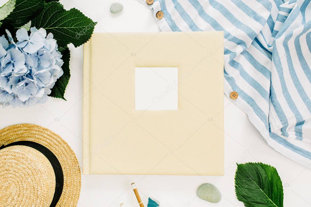Family wedding photo album with blank space, blue hydrangea flower bouquet, striped blanket, straw hat, decoration on white background. Flat lay, top view.
