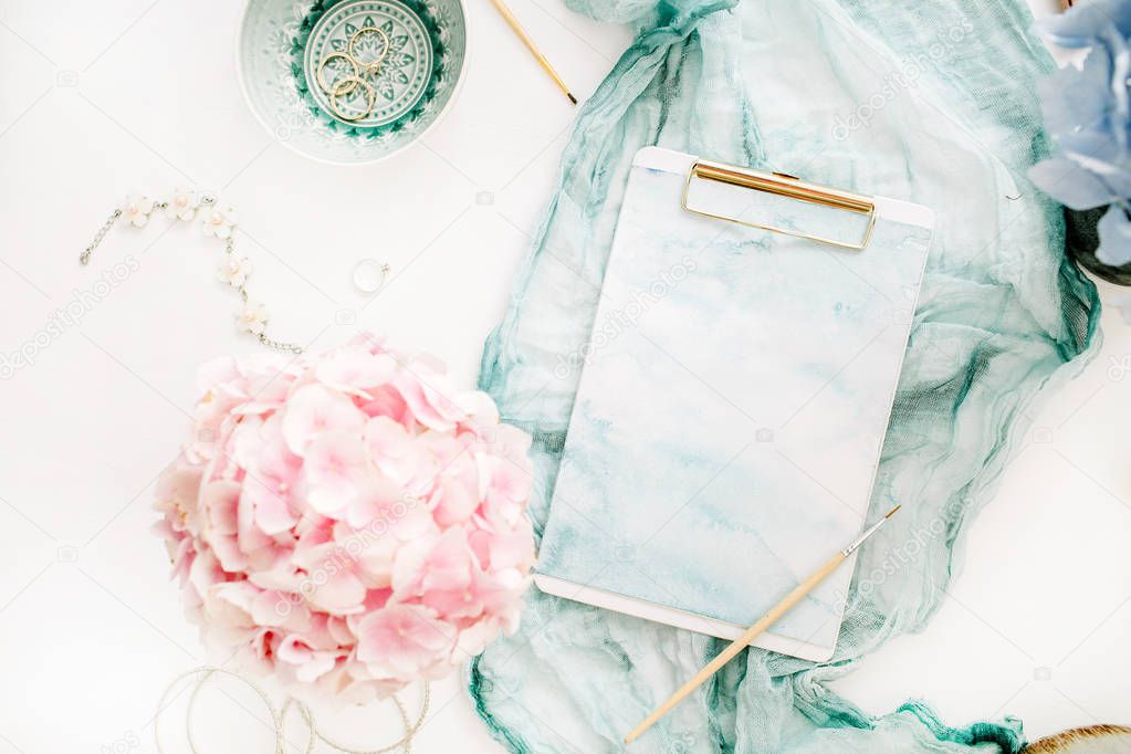 Artist home office desk workspace with watercolor clipboard, paintbrush, turquoise blanket, colorful pastel hydrangea flower bouquet, woman fashion accessories on white background. Flat lay, top view mockup.