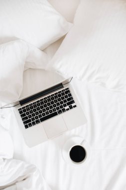 Laptop ve kahve beyaz keten ile yatakta. Serbest blogger çalışma alanı düz yatıyordu. Üstten görünüm en az arka plan.