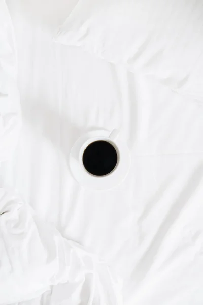 Cup of coffee on clean white linens. Flat lay, top view minimalist background.