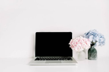 Boş ekran laptop ve pembe ve mavi ortanca çiçek buketleri beyaz arka plan üzerinde. Çok az ev ofis resepsiyon çalışma alanı.