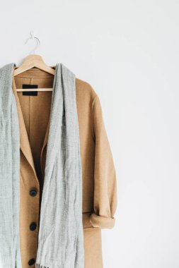 Bej renkli yün kadın ceket ve beyaz duvar askı üzerinde gri eşarp. Kadın moda kış bez kavramı.