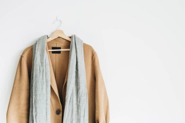 Bej renkli yün kadın ceket ve beyaz duvar askı üzerinde gri eşarp. Kadınsı moda kış bez butik konsept.