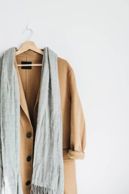 Bej renkli yün kadın ceket ve beyaz duvar askı üzerinde gri eşarp. Kadınsı moda kış bez butik konsept.