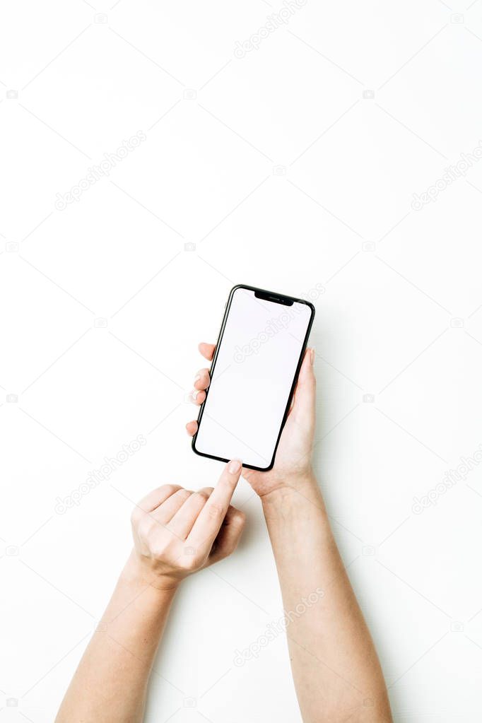 Woman hand touching blank smart phone screen. Flat lay, top view mock up template.