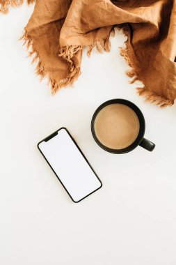 Bir fincan kahve süt, kahverengi battaniye, boş ekran mockup beyaz arka plan üzerinde ile akıllı telefon. Düz yatıyordu, en iyi görünümü.