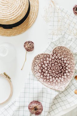 Flatlay kompozisyon pembe el yapımı kalpli battaniye, gül çiçek ve hasır şapka plaka beyaz arka plan üzerinde tarz. Düz yatıyordu, en iyi görünümü.