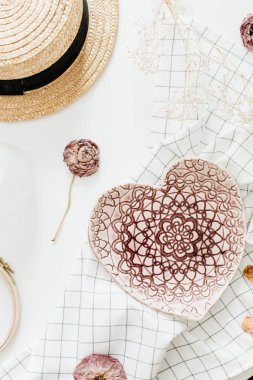Flatlay kompozisyon pembe el yapımı kalpli tabak, gül çiçek ve hasır şapka beyaz arka plan üzerinde tarz. Düz yatıyordu, en iyi görünümü.