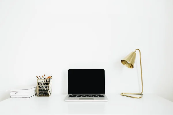 Home office desk workspace with laptop, golden lamp, stationery on white background. Minimalist modern interior design concept. Desktop mock up.