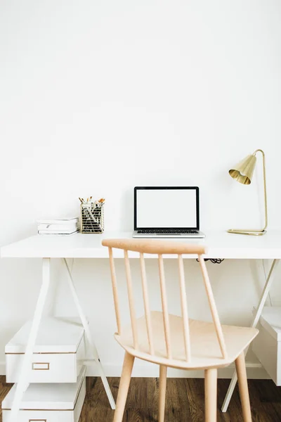 Home office desk workspace. Laptop with blank screen mock up, golden lamp, stationery on white desktop. Modern Scandinavian interior design concept.