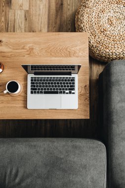 Düz ev ofis resepsiyon workspace ile yatıyordu. Laptop, kahve fincanı üzerinde ahşap masa, kanepe. Üstten görünüm modern iç tasarım konsepti.