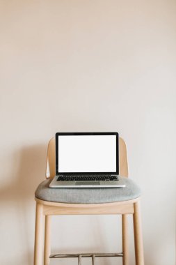 Dizüstü bilgisayar ekranı pastel bej renkli arka plan üzerinde ahşap sandalye üzerinde sahte ile. Blog, Web sitesi, sosyal medya kahraman üstbilgi şablonu.