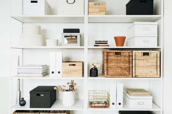 Modern home office cabinet interior design concept. White storage shelves with boxes, eucalyptus, decorations. Scandinavian style room.