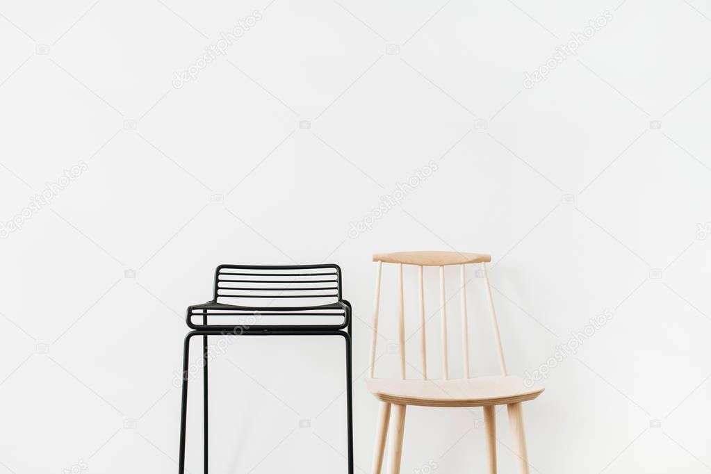 Black metal stool, wooden chair at white wall. Modern minimal Scandinavian furniture design concept.