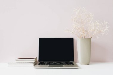 Dizüstü bilgisayar ve çiçek buketi pembe arka plan üzerinde. Ön görünüm minimal modern ev ofis masası çalışma alanı. Boş ekran kahraman başlığı kadar alay. Blog, sosyal medya, web sitesi şablonu. Kız patron kavramı.