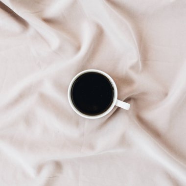 İpek pembe battaniyenin üzerine kahve bardağı. Minimal düz döşeme, üst görünüm arka plan.