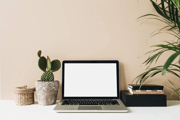 Minimalist home office desk workspace with laptop, cactus, palm on beige background. Front view copy space blank mock up. Freelancer business template.