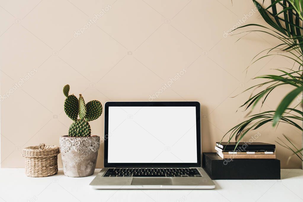 Minimalist home office desk workspace with laptop, cactus, palm on beige background. Front view copy space blank mock up. Freelancer business template.