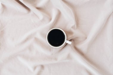 İpek pembe battaniyenin üzerine kahve bardağı. Minimal düz döşeme, üst görünüm arka plan.