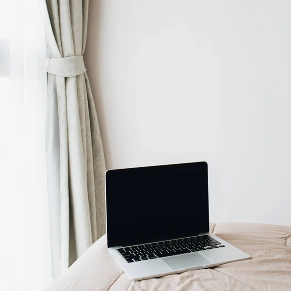 Laptop on bed. Minimal interior design concept. Freelancer business at home concept. Blank screen copy space mock up.