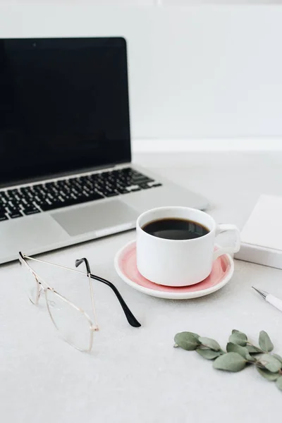 Minimalist home office desk workspace. Laptop, coffee, glasses, notebook, eucalyptus.