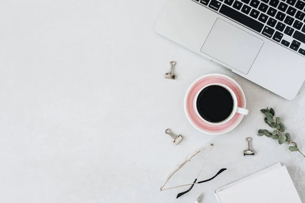 Minimalist home office desk workspace. Laptop, coffee, glasses, notebook, eucalyptus on blank background. Flat lay, top view girlboss concept.