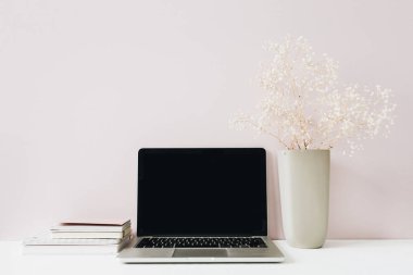 Dizüstü bilgisayar ile minimalist ev ofis masası çalışma alanı, pembe arka plan üzerinde çiçek buketi. Boş kopyalama alanı olan ön görünüm kahraman üstbilgisi.